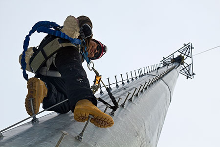 Cell tower service worker climbing upward wearing saftey gear.