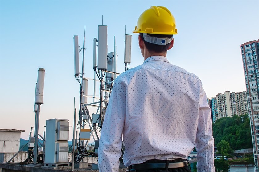 Man with yellow hard hat looking at radio tower installed on top of a building.